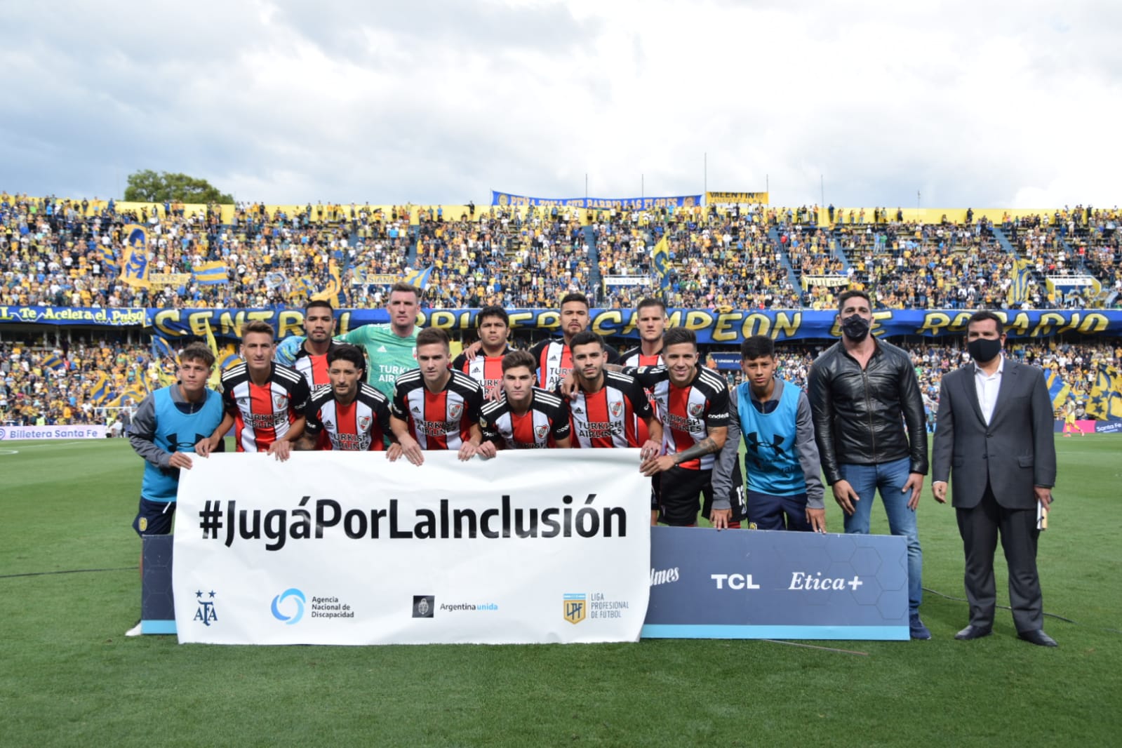 Imágen de los jugadores de River y de Fernando Galarraga en el campo de juego, sosteniendo la bandera con el lema #JugáPorLaInclusión.