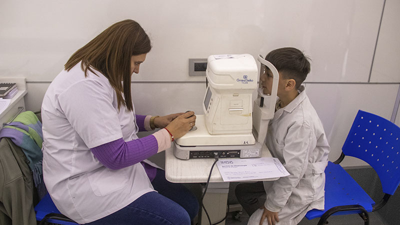 El profesional a cargo está haciendo uso del equipo oftalmológico mientras le hace un examen visual a un nene de la escuela.