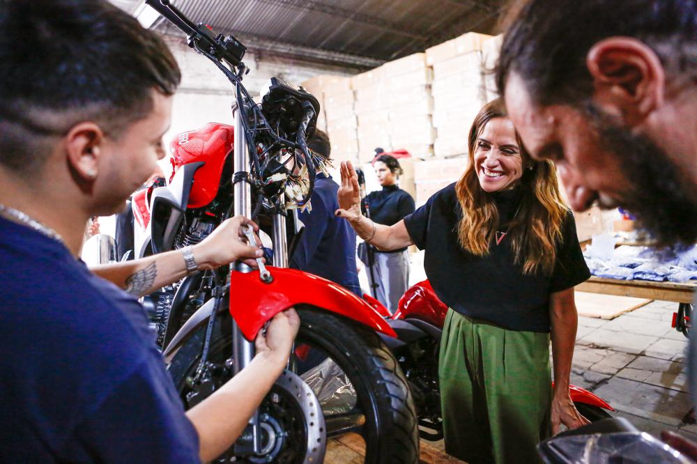 La ministra junto a una moto color rojo en el depósito del taller de motos Dropped Pin. 