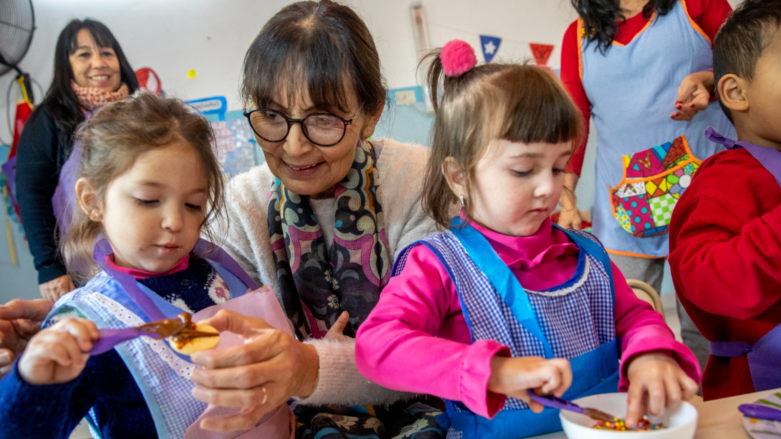 Abuela con dos nenas en el jardín de infantes participando de la actividad que consitía en el armando de alfajores de maicena.